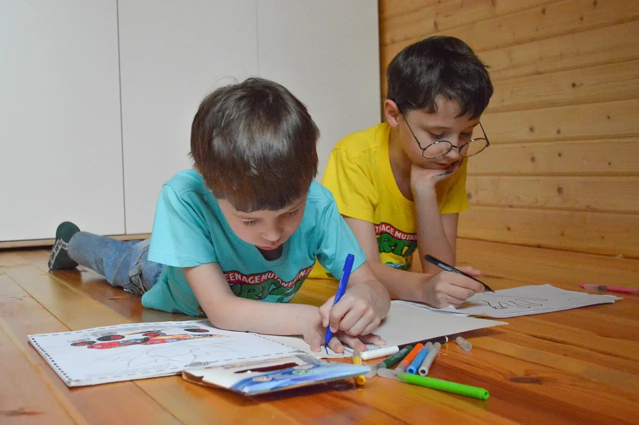 Dzieci rysujące na podłodze, jedno w okularach